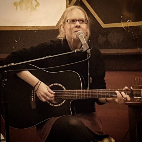 Jessica Mahnke sitzt mit Gitarre in einem gemütlichen Pub und singt